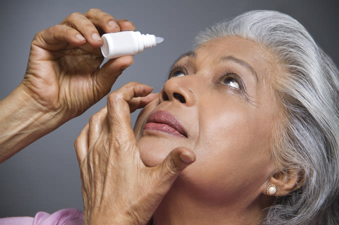 An older Indian woman putting eye drops in her eye.